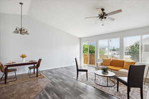 Living room featuring lofted ceiling, a chandelier, wood finished floors, a ceiling fan, and a textured ceiling