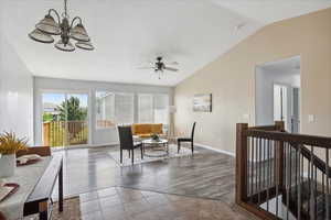 Living area with vaulted ceiling, ceiling fan, a chandelier, wood finished floors, and an upstairs landing