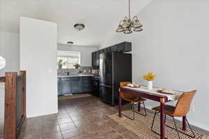 Kitchen with freestanding refrigerator, vaulted ceiling, black range with gas stovetop, backsplash, and a chandelier