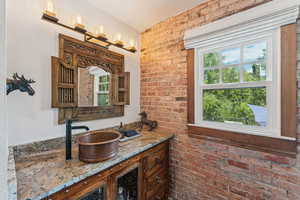 Bathroom with healthy amount of natural light, vanity, and brick wall