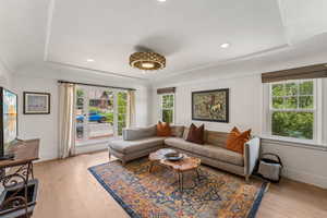 Living area with a raised ceiling, light wood-style flooring, and recessed lighting