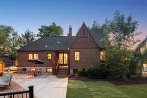Back of property at dusk with brick siding, a patio area, a chimney, and outdoor dining space