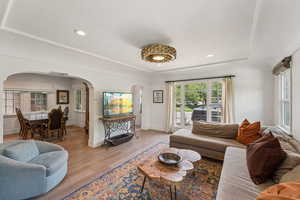 Living area with arched walkways, light wood finished floors, recessed lighting, and a tray ceiling