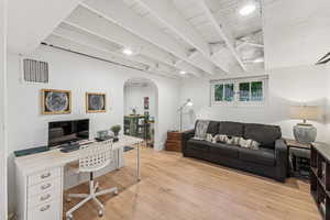 Office area featuring arched walkways, light wood-style floors, and beamed ceiling