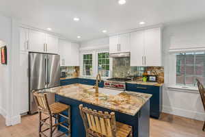 Kitchen featuring stainless steel appliances, under cabinet range hood, light wood finished floors, a kitchen bar, and recessed lighting