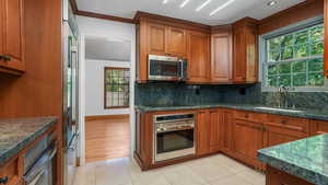 Kitchen with appliances with stainless steel finishes, brown cabinets, decorative backsplash, crown molding, and light tile patterned floors