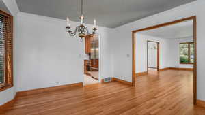 Empty room with light wood-type flooring, a chandelier, and ornamental molding