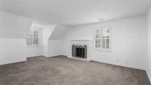 Unfurnished living room featuring carpet and a fireplace with raised hearth