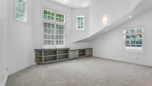 Unfurnished living room featuring light carpet, healthy amount of natural light, recessed lighting, and a towering ceiling