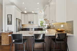 Kitchen featuring appliances with stainless steel finishes, a peninsula, white cabinetry, dark wood-style floors, and recessed lighting