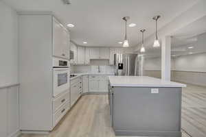 Kitchen with appliances with stainless steel finishes, wainscoting, light countertops, a kitchen island, and decorative light fixtures