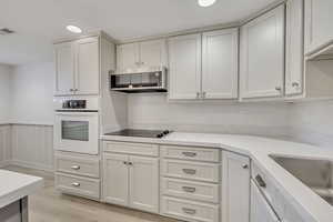Kitchen with white oven, exhaust hood, light wood-style floors, black electric stovetop, and light stone counters