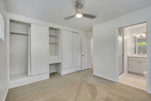 Unfurnished bedroom with two closets, light colored carpet, ensuite bath, an office area, and ceiling fan