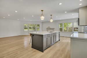 Kitchen with gray cabinets, recessed lighting, light wood finished floors, pendant lighting, and an island with sink