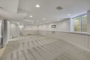 Basement featuring wainscoting, light carpet, recessed lighting, and stainless steel refrigerator