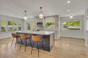Kitchen with stainless steel microwave, light wood-style floors, light countertops, a kitchen island with sink, and a kitchen bar