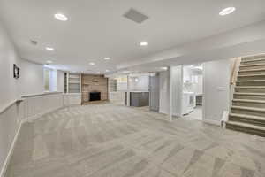 Unfurnished living room featuring recessed lighting, light carpet, stairway, a fireplace, and healthy amount of natural light
