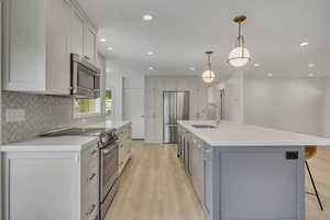 Kitchen featuring appliances with stainless steel finishes, tasteful backsplash, light wood-type flooring, a kitchen breakfast bar, and recessed lighting