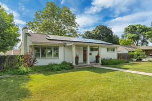 View of front of property featuring solar panels, a chimney, brick siding, covered porch, and roof with shingles