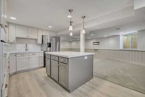Kitchen featuring gray cabinets, light countertops, light wood-style flooring, wainscoting, and pendant lighting