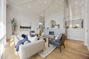Living area with high vaulted ceiling, light wood-type flooring, stairway, a fireplace, and recessed lighting