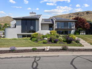 Contemporary house featuring a balcony, a standing seam roof, a mountain view, solar panels, and stucco siding