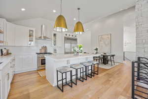 Kitchen with wall chimney exhaust hood, premium appliances, a breakfast bar, white cabinetry, and a center island