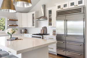 Kitchen featuring built in fridge, wall chimney exhaust hood, open shelves, white cabinets, and vaulted ceiling