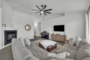 Carpeted living room with a ceiling fan, lofted ceiling, a tile fireplace, and healthy amount of natural light