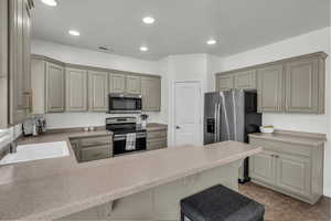 Kitchen with appliances with stainless steel finishes, a peninsula, gray cabinetry, a breakfast bar, and recessed lighting