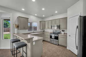 Kitchen with appliances with stainless steel finishes, a peninsula, gray cabinetry, a breakfast bar area, and light tile patterned floors