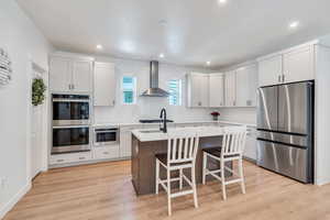 Kitchen with stainless steel appliances, wall chimney range hood, decorative backsplash, a center island with sink, and light countertops