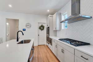 Kitchen with wall chimney range hood, appliances with stainless steel finishes, light wood-style floors, backsplash, and light countertops