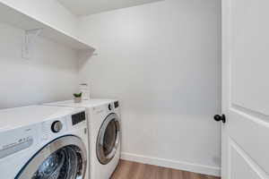 Washroom with washing machine and dryer and light wood-style flooring