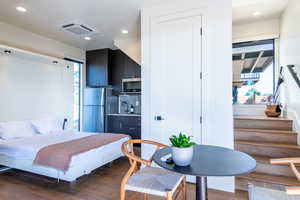 Bedroom with freestanding refrigerator, wood finished floors, recessed lighting, and bar with sink