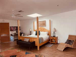 Bedroom featuring wood finished floors, a skylight, a textured wall, and a ceiling fan