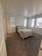 Bedroom featuring a textured ceiling, dark colored carpet, and baseboards