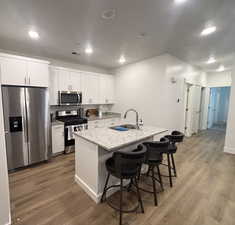 Kitchen featuring stainless steel appliances, a sink, light wood finished floors, a breakfast bar, and white cabinets