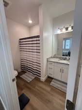 Bathroom featuring vanity, wood finished floors, toilet, a shower with shower curtain, and baseboards