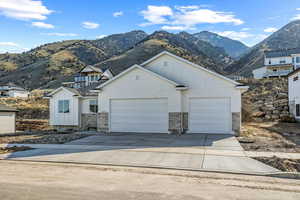 View of front of home with board and batten siding, an attached garage, concrete driveway, a mountain view, and stone siding