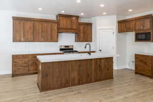 Kitchen featuring stainless steel range, black microwave, light countertops, premium range hood, and a center island with sink