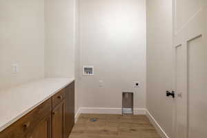Washroom with light wood-style floors, hookup for an electric dryer, washer hookup, and cabinet space