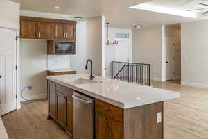 Kitchen with dishwasher, light wood-type flooring, a kitchen island with sink, light countertops, and a chandelier