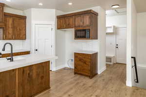 Kitchen featuring black microwave, light countertops, decorative backsplash, recessed lighting, and light wood-style flooring