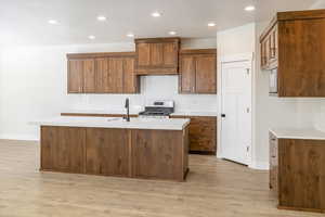 Kitchen featuring stainless steel range, light wood-style floors, light countertops, backsplash, and recessed lighting