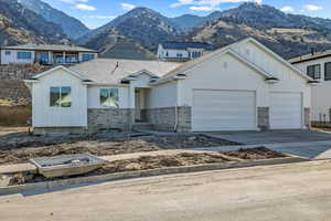 View of front facade with board and batten siding, an attached garage, driveway, a mountain view, and stone siding