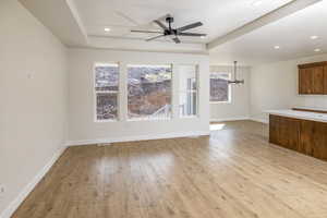 Unfurnished living room with a raised ceiling, light wood-style floors, ceiling fan, and recessed lighting