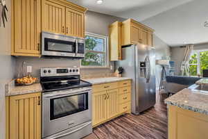 Kitchen featuring appliances with stainless steel finishes, dark wood-type flooring, cream cabinetry, recessed lighting, and granite countertops