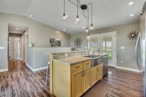 Kitchen with stainless steel appliances, cream cabinets, dark wood finished floors, vaulted ceiling, and a kitchen island with sink