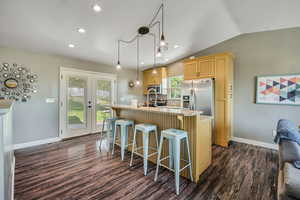 Updated Kitchen featuring appliances with stainless steel finishes, dark wood-style flooring, a kitchen bar, vaulted ceiling, and a kitchen island with sink